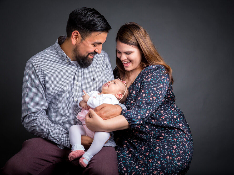 A man and woman hold a baby in front of a gray background